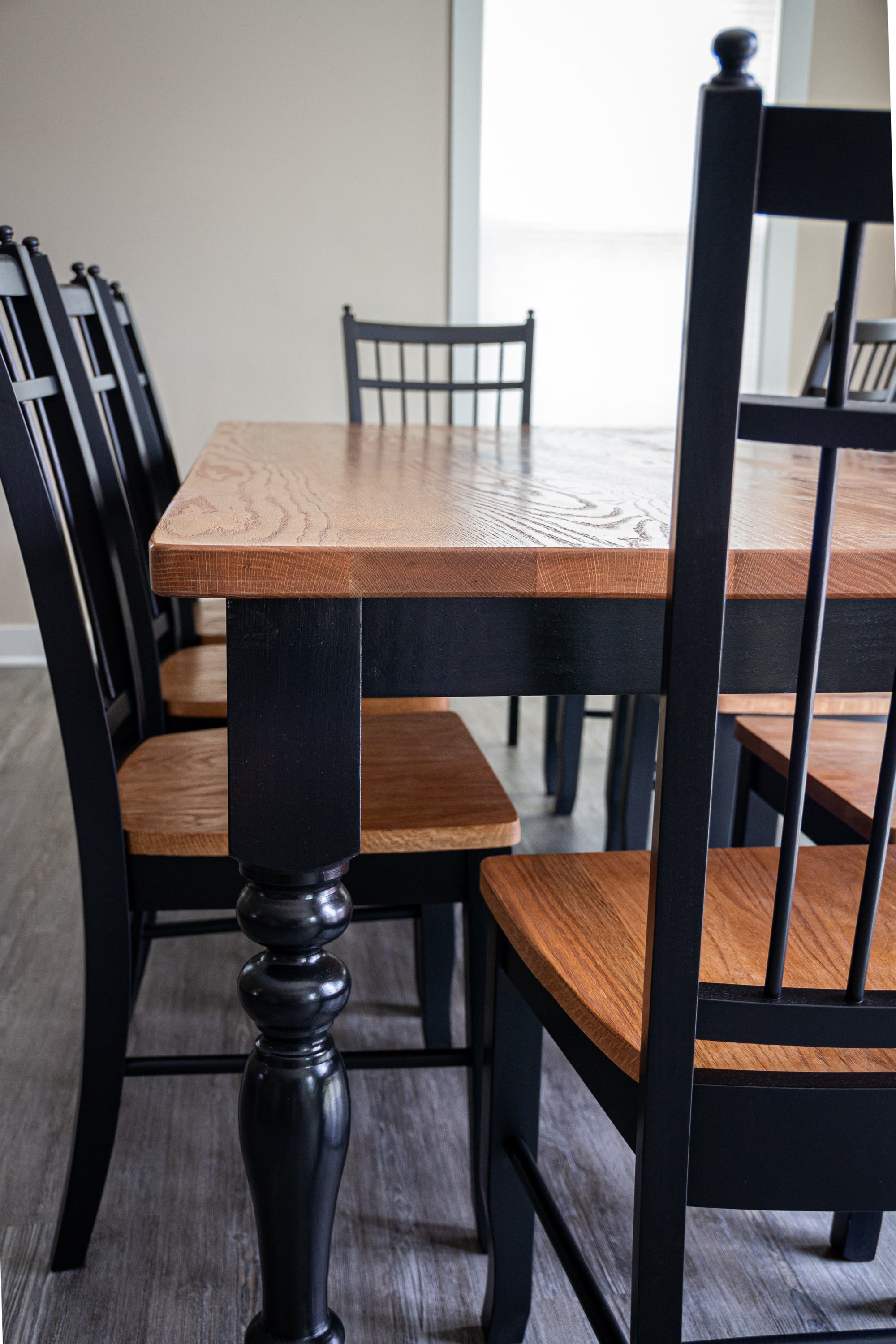 A black dining table with a warm medium-brown wood top and matching wood chair seats, surrounded by black wooden chairs in a dining room setting.