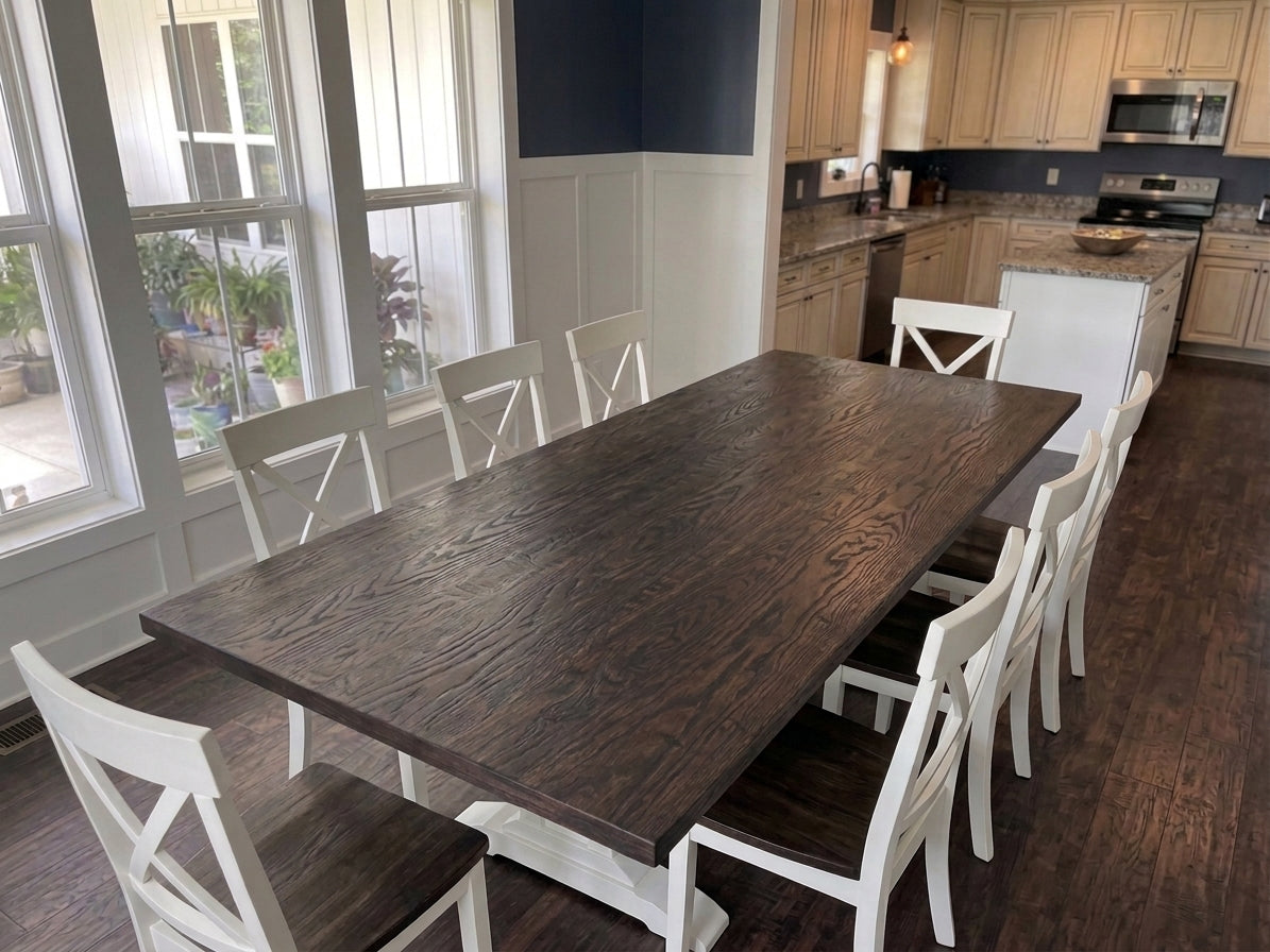 A dark brown wooden dining table with eight white chairs, set in a bright dining room with hardwood floors and a modern kitchen in the background.